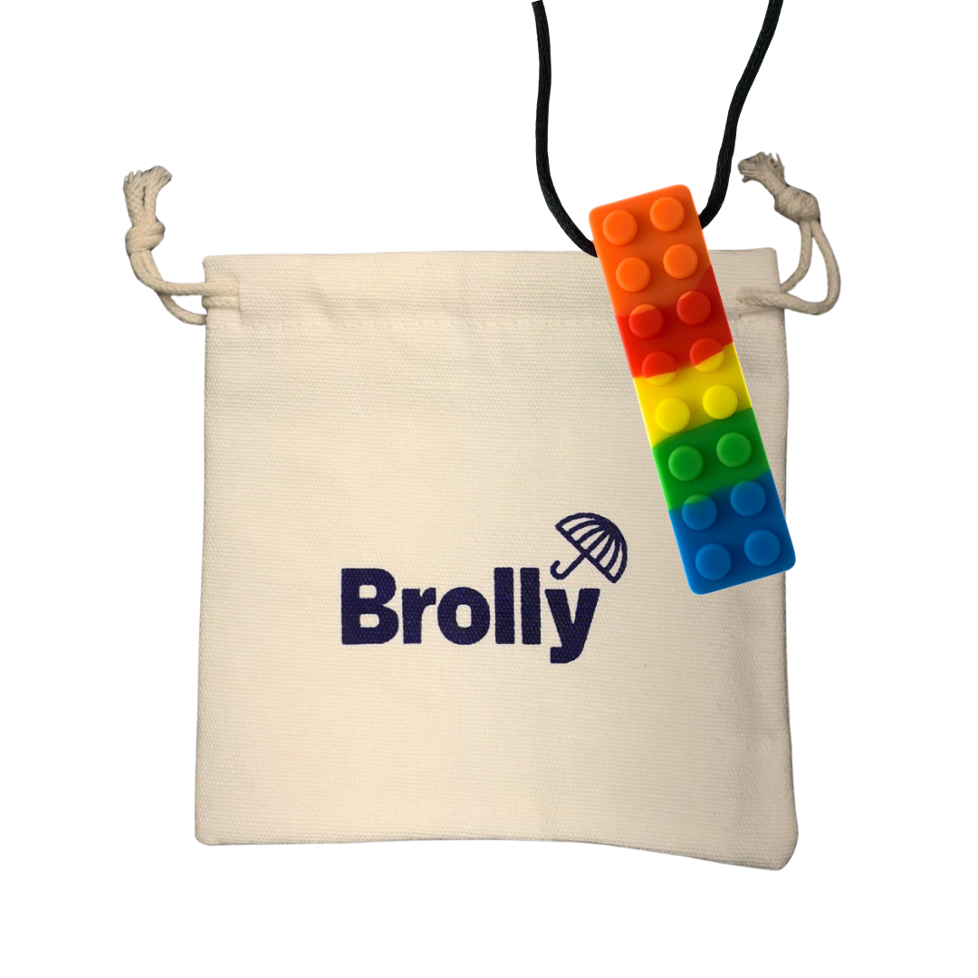 Beige drawstring pouch and brick-shaped Brolly Sheet Chew Necklace on a black cord against a white background - Rainbow