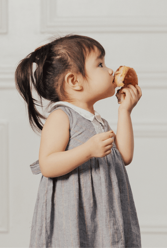 A small toddler girl eating a donut and looking upwards in her home