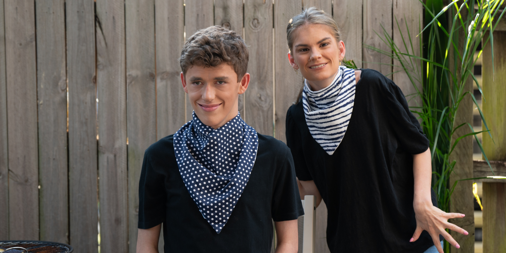 Teenage boy and young woman modeling Blue/White Polka Dot and Navy Stripes waterproof Cotton Bandana Bibs from the Cerebral Palsy Society collection, smiling outdoors.ive clothing collection.