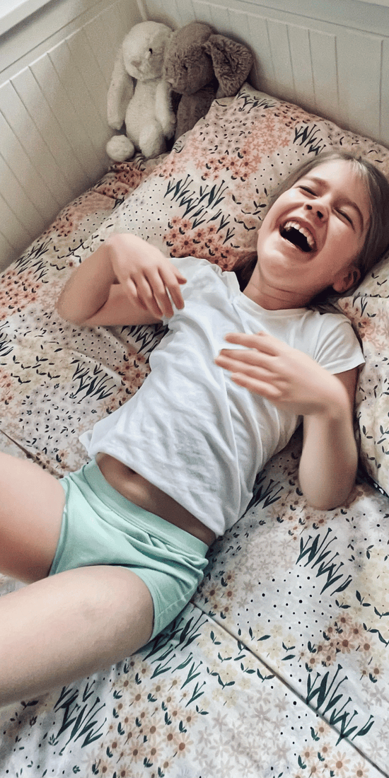 Young girl laughing on a bed wearing Organic Night Training Pants from Snazzi Pants