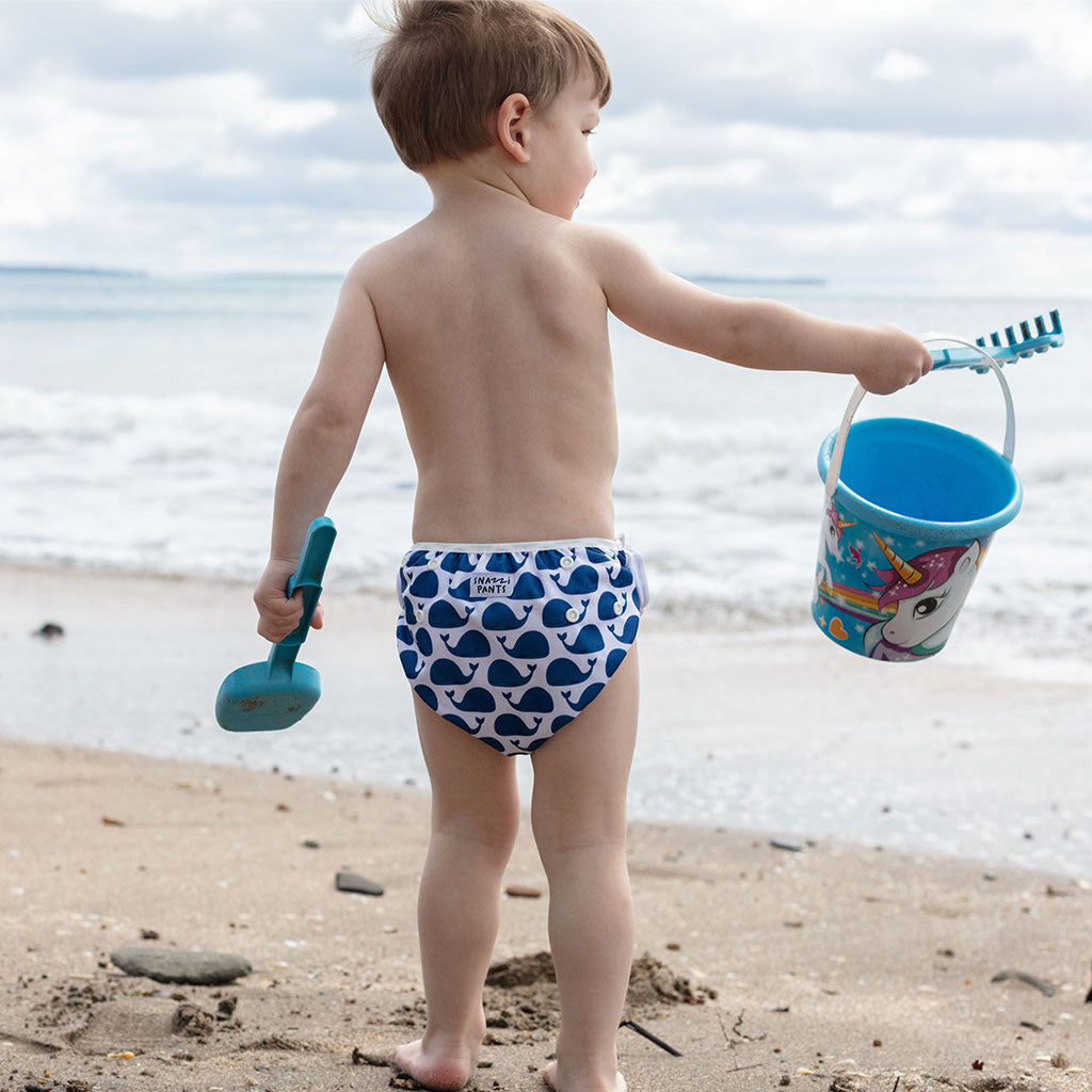 Child on a beach wearing blue whale-patterned swim diapers with a bucket and shovel - Whales